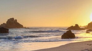 Uma praia com pedras grandes e ondas ao pôr do sol.
