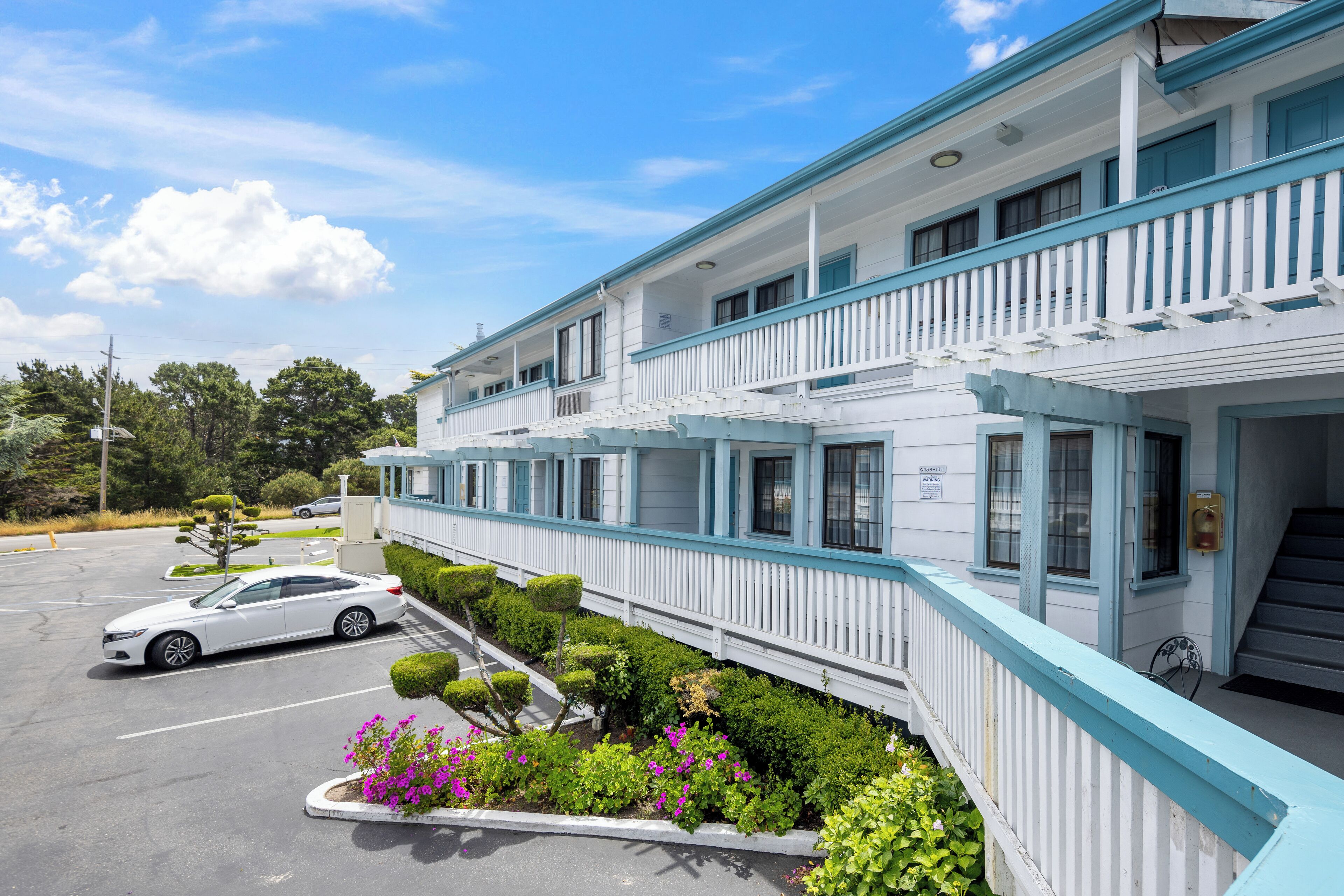 A two-story hotel with a white exterior and blue accents, featuring a parking lot and well-maintained landscaping.