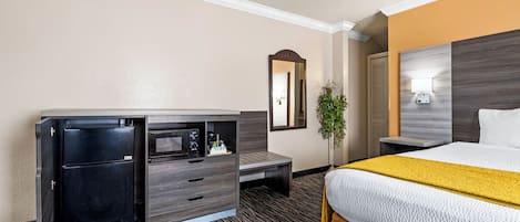 Una habitación de hotel con cama, escritorio, computadora, refrigerador pequeño y espejo.