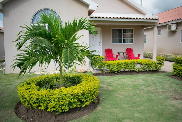 A house with a well-maintained lawn, a palm tree, and two red chairs on the porch.