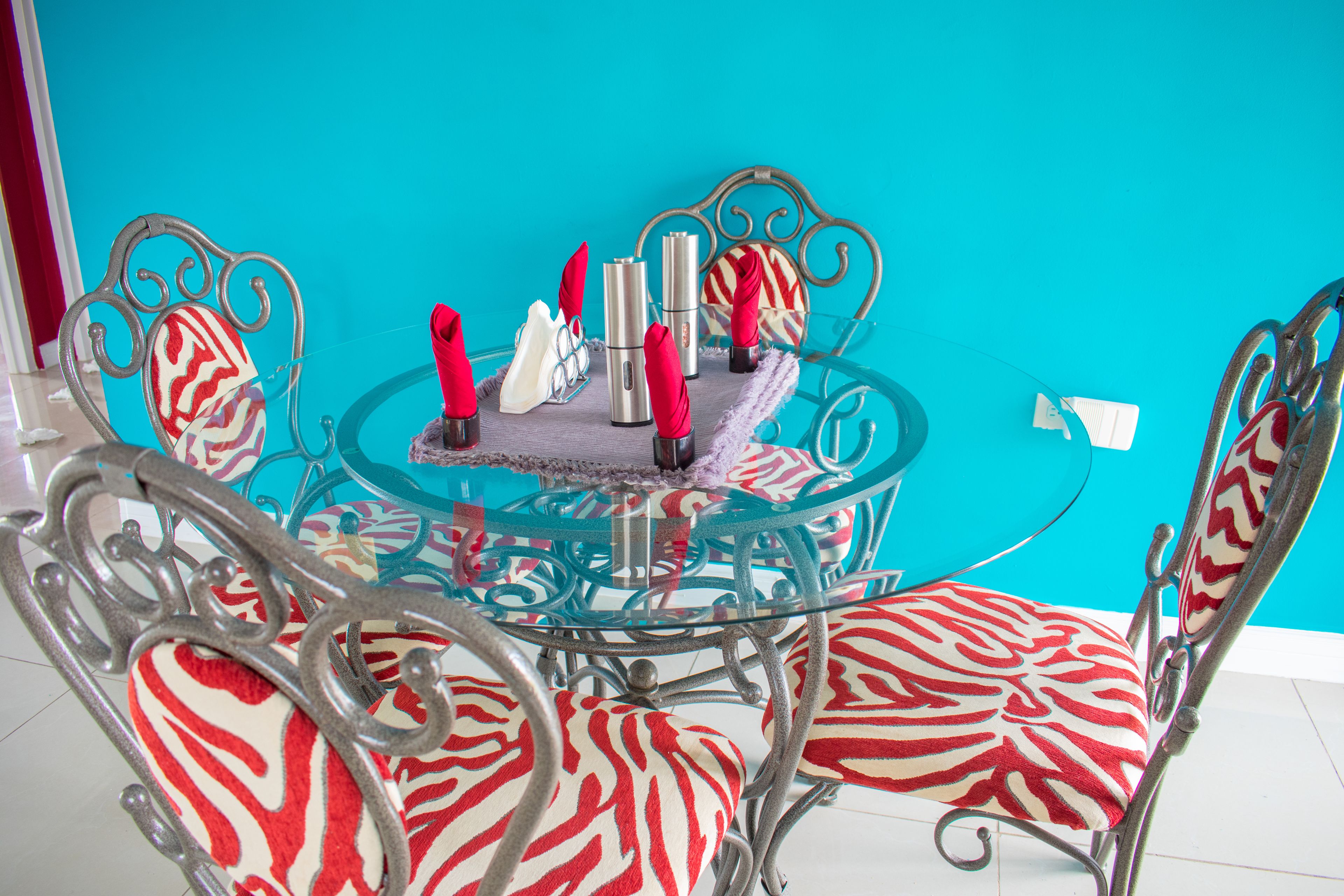 A dining area with a glass table and zebra-patterned chairs, set against a turquoise wall.