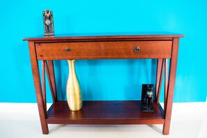 A wooden console table with two drawers and a shelf, against a blue wall.