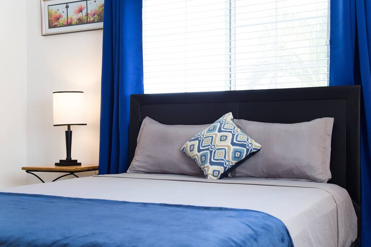 Un letto rifatto con cura, un cuscino decorato, una lampada da comodino e un quadro appeso alla parete.
