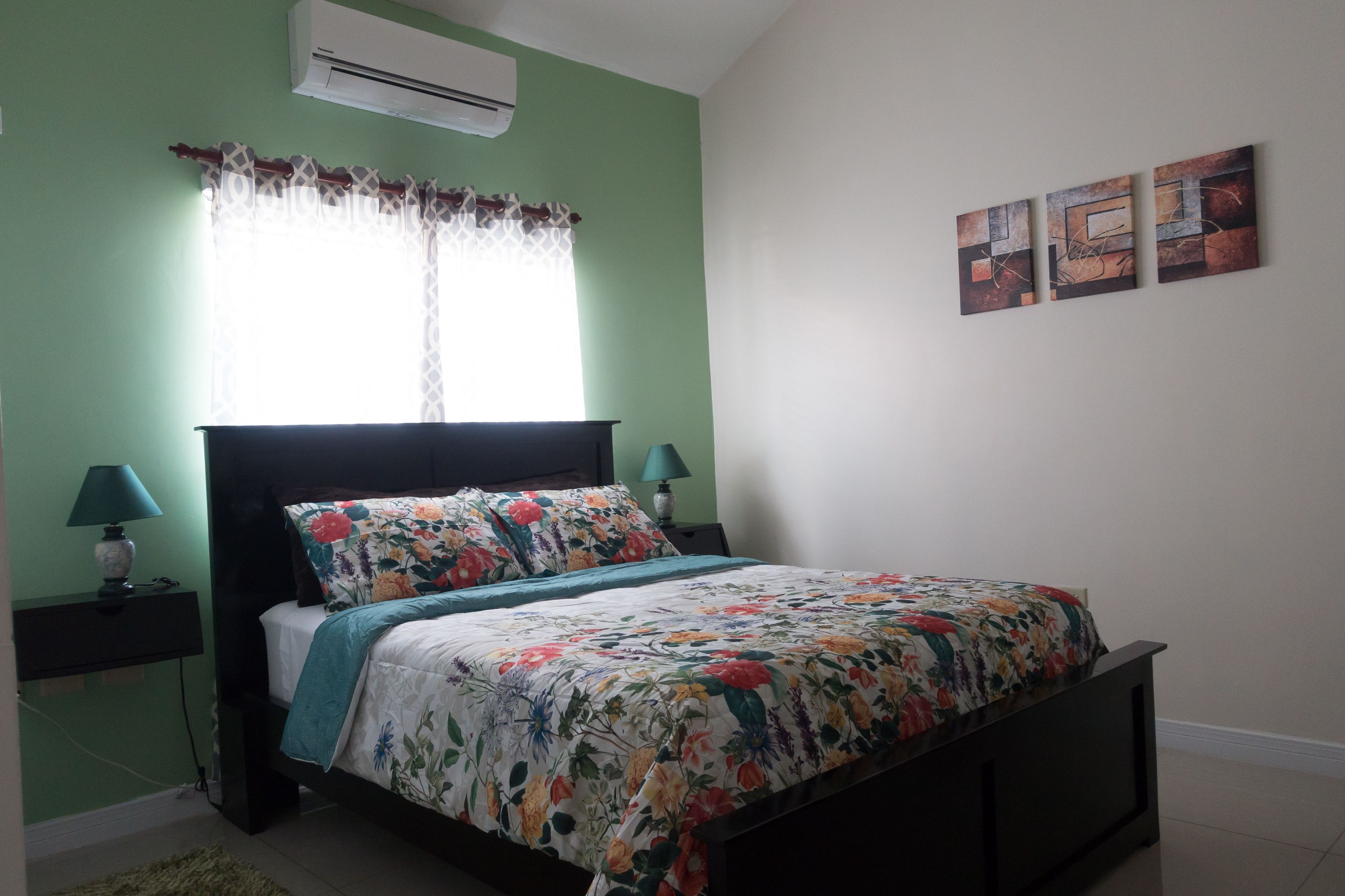 A bedroom with a bed, nightstands, a window with curtains, and wall art.