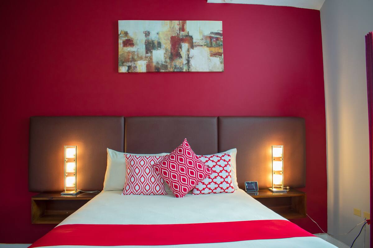 Camera d'albergo con parete rossa, un letto grande con lenzuola bianche e due comodini con lampade.