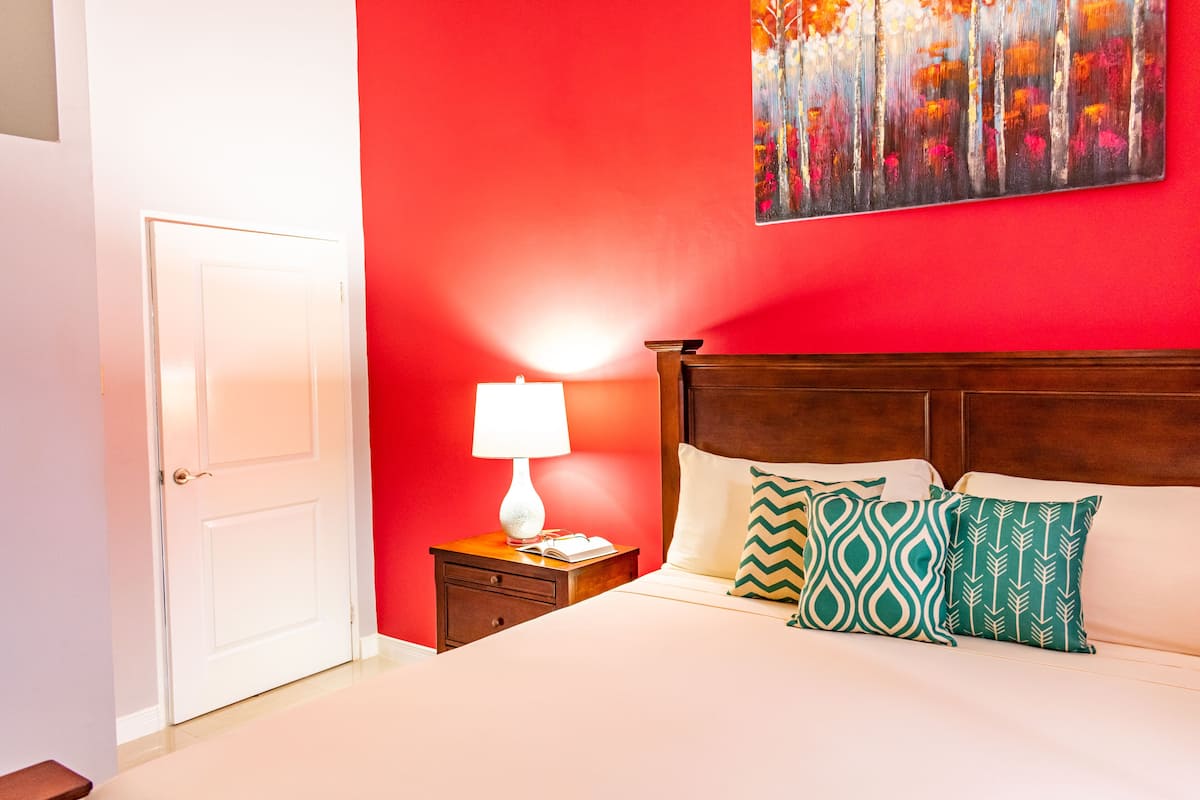 Una camera d'albergo con una parete rossa, una testiera in legno e un letto con cuscini a motivi.