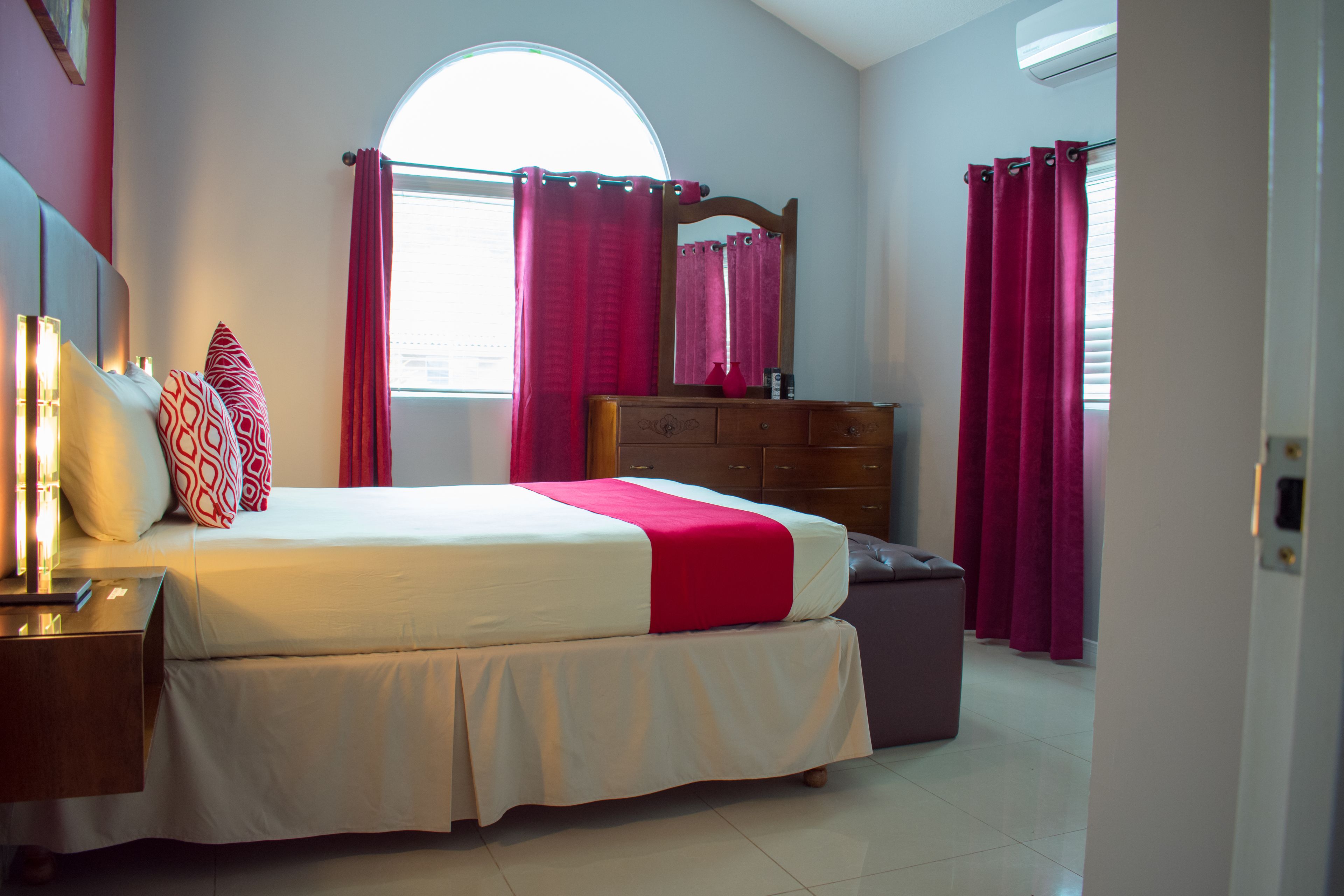 A bedroom with a bed, nightstands, a dresser, and a window with curtains.