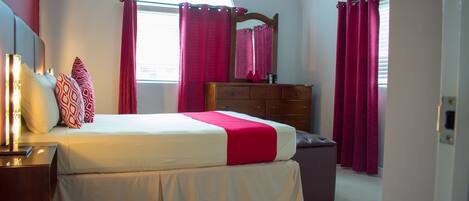 A bedroom with a bed, nightstands, a dresser, and a window with curtains.