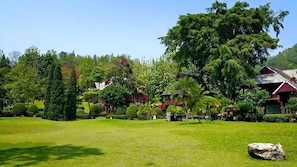 A lush garden with a variety of trees and shrubs, a well-maintained lawn, and traditional red-roofed buildings. - Baanklangdoi Resort (Hang Dong)