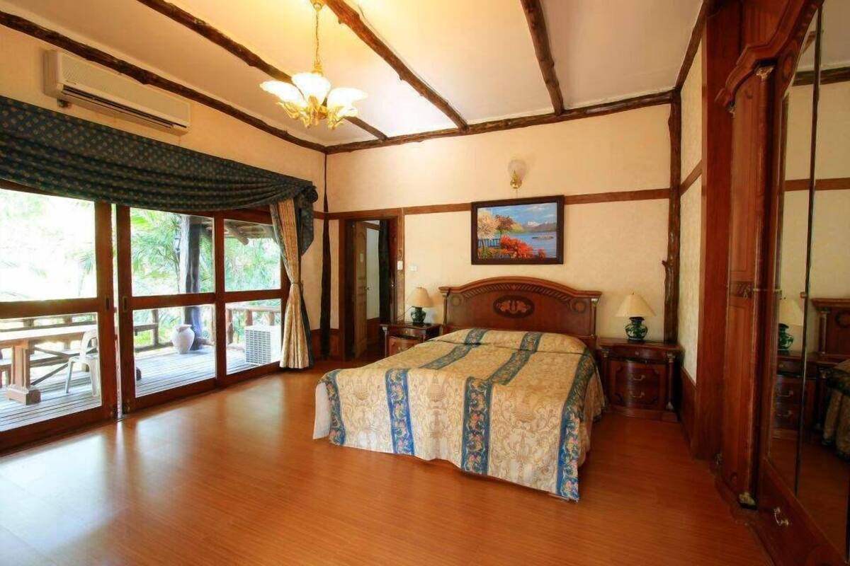 Un dormitorio amplio con una cama grande, suelo de madera, ventilador de techo y vistas a un área exterior a través de puertas de vidrio.
