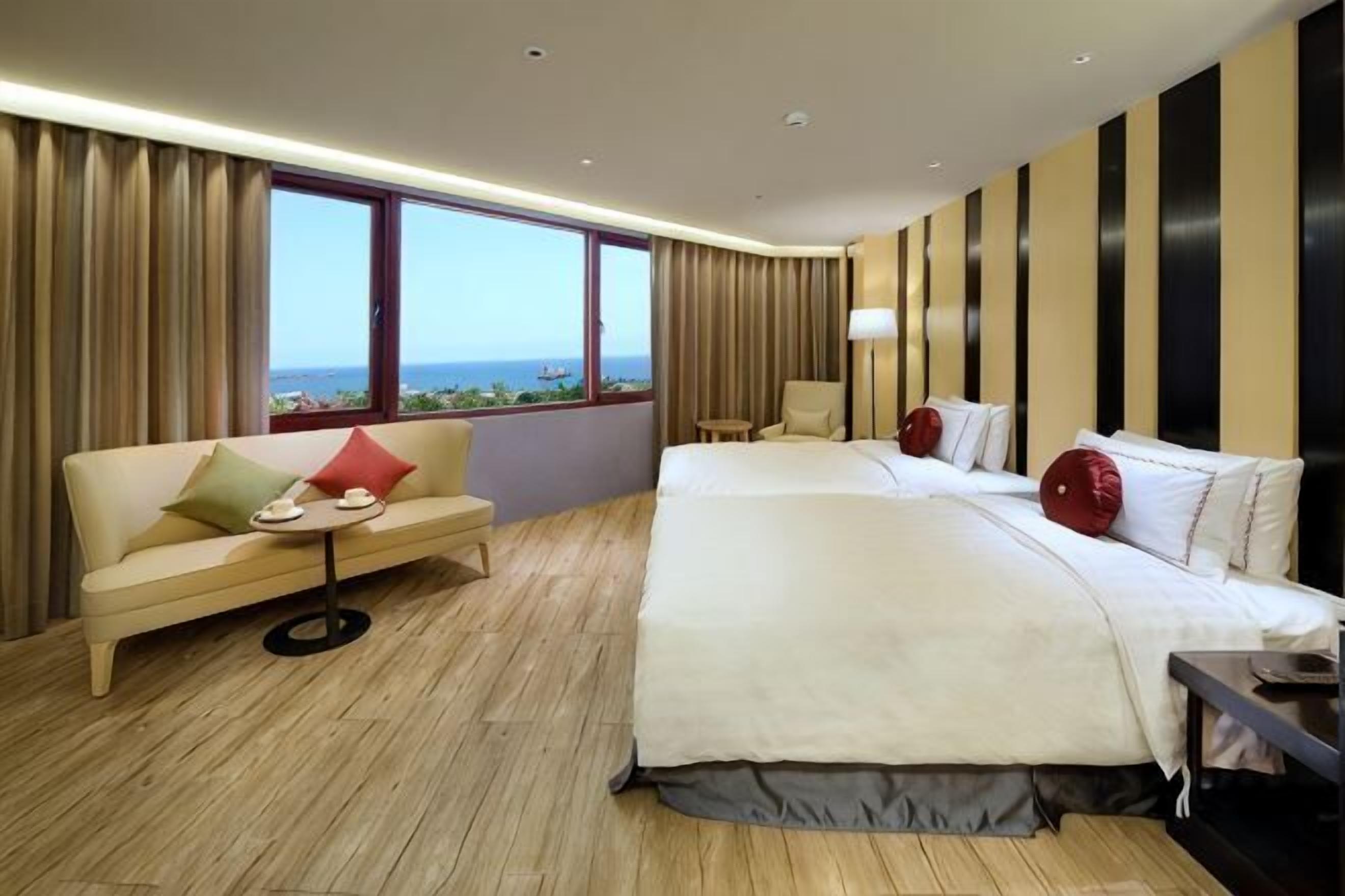 A hotel room with a bed, a sofa, a small table, and a view of the ocean.