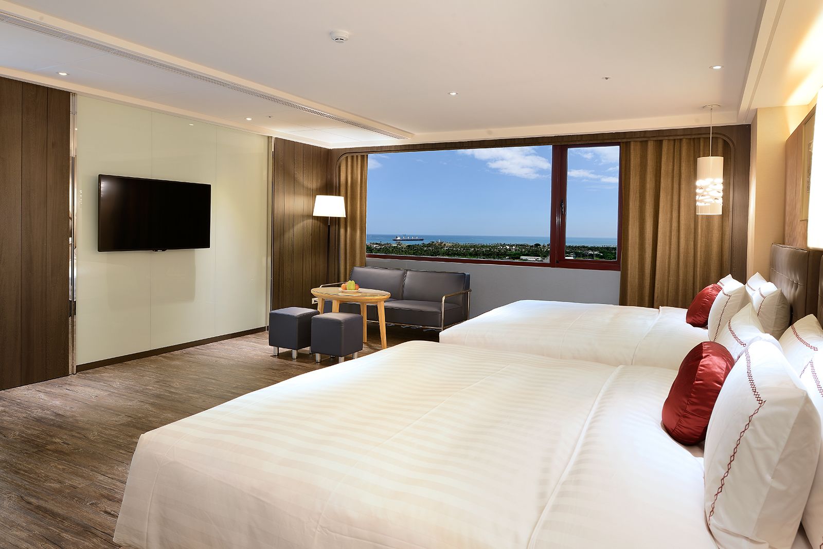 A hotel room with a large bed, a TV, a desk with a chair, and a view of the ocean.
