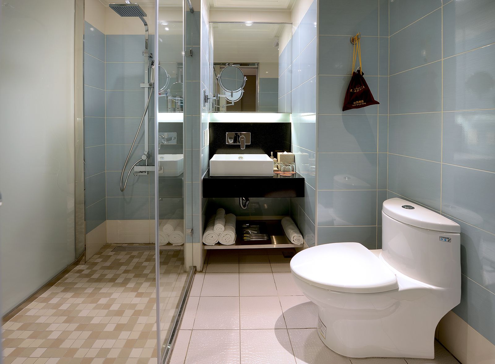 A modern bathroom with a glass-enclosed shower, a white toilet, and a sink area with towels and toiletries.