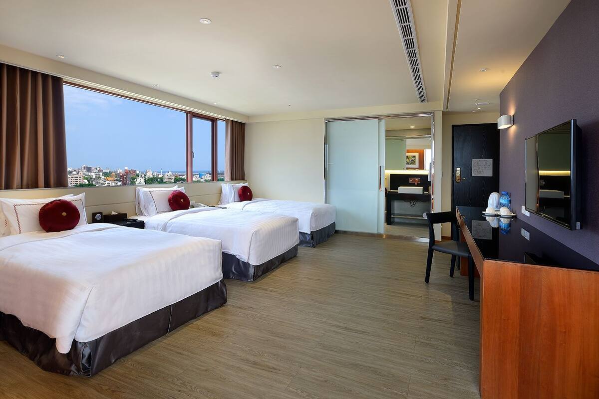 A hotel room with two beds, a desk, and a TV.
