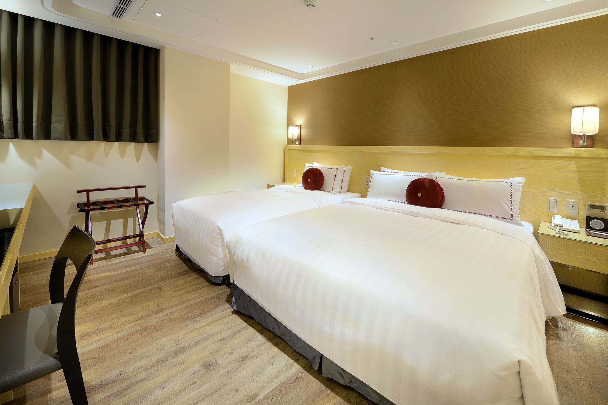A hotel room with two beds, a desk, a chair, and a bedside table with a phone and a radio.