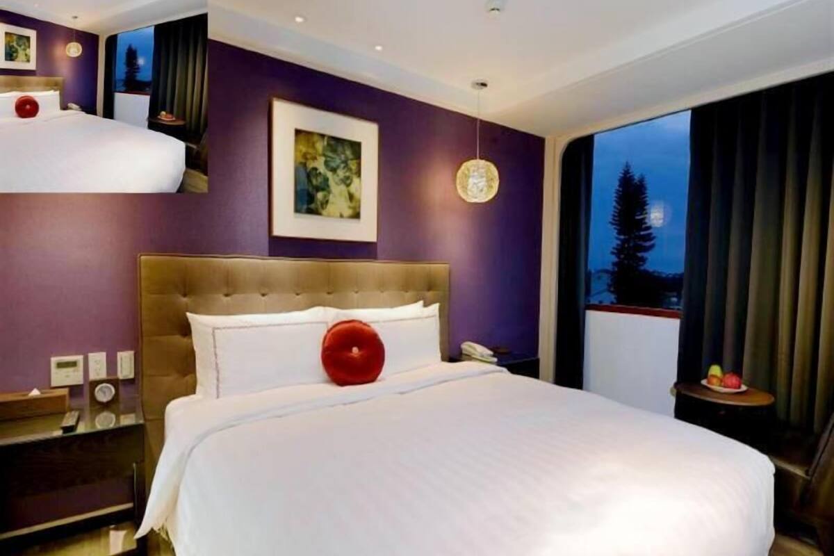 A modern hotel room with a large bed, a nightstand, a painting on the wall, and a view of the night sky.