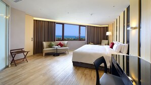 A hotel room with a large bed, a sofa, a small table, and a chair. There is a window with a view of the sea. - Shiny Ocean Hotel (Hualien City)