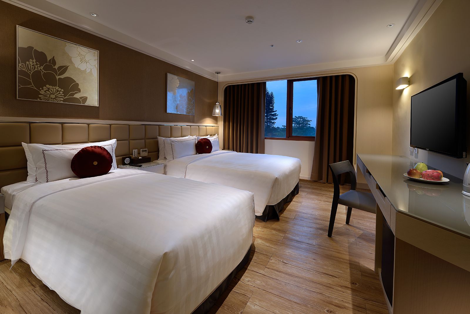 A hotel room with two beds, a desk with a TV, and a window with curtains.