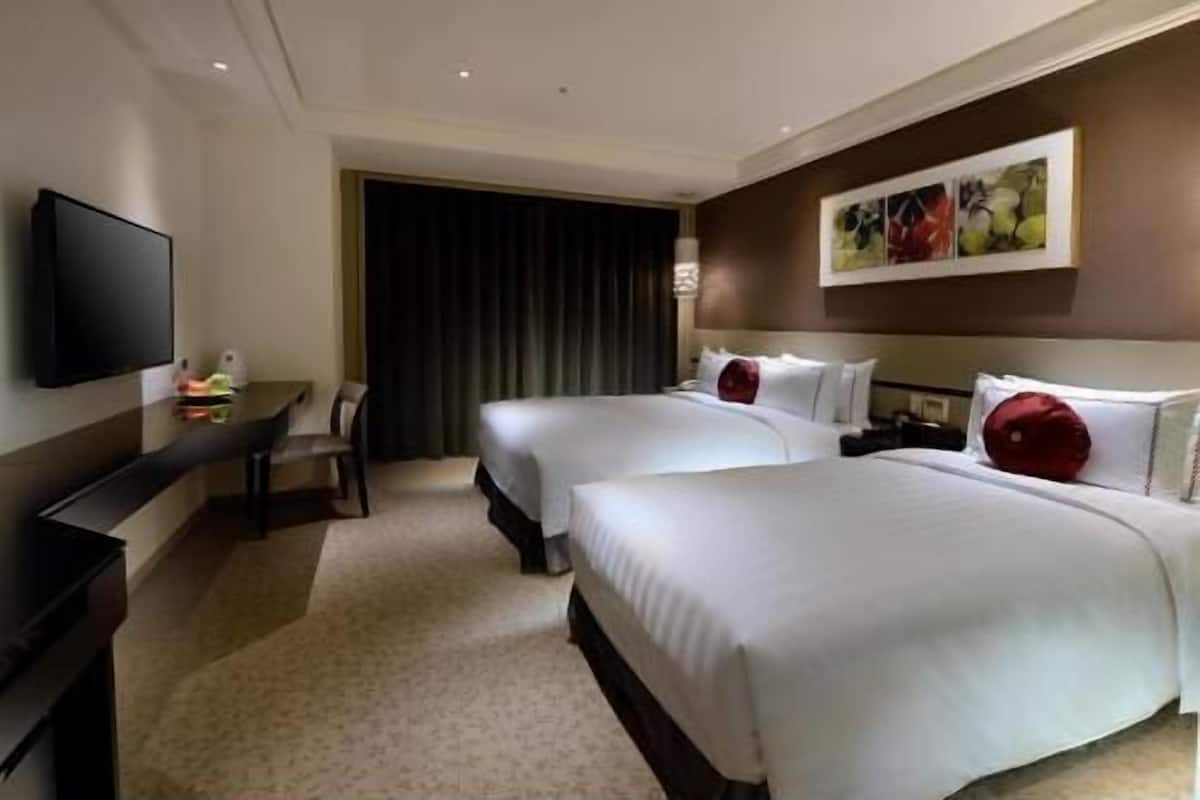 A hotel room with two beds, a flat-screen TV, a desk, and a large window with curtains.