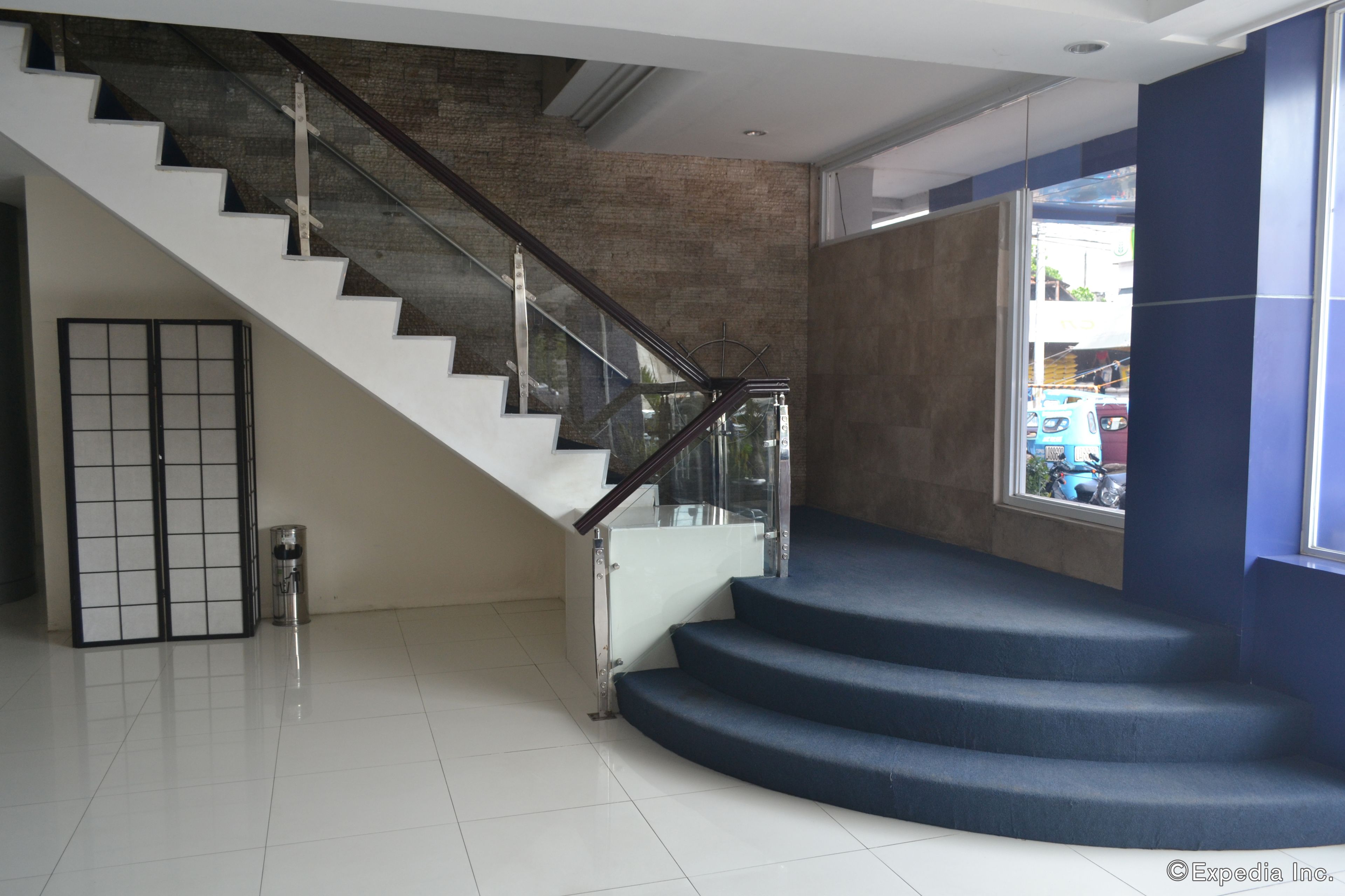 Un escalier moderne avec des rampes en verre et des marches recouvertes d’une moquette bleue, menant à une pièce dotée d’une grande fenêtre et offrant une vue sur l’extérieur.