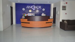 A hotel reception desk with a blue wall featuring the hotel name and a clock. - Anchor Hotel (General Santos)