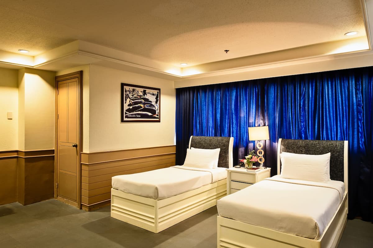 Ein Hotelzimmer mit zwei Einzelbetten, einem Nachttisch mit Lampe, einem gerahmten Bild an der Wand und einem blauen Vorhang.