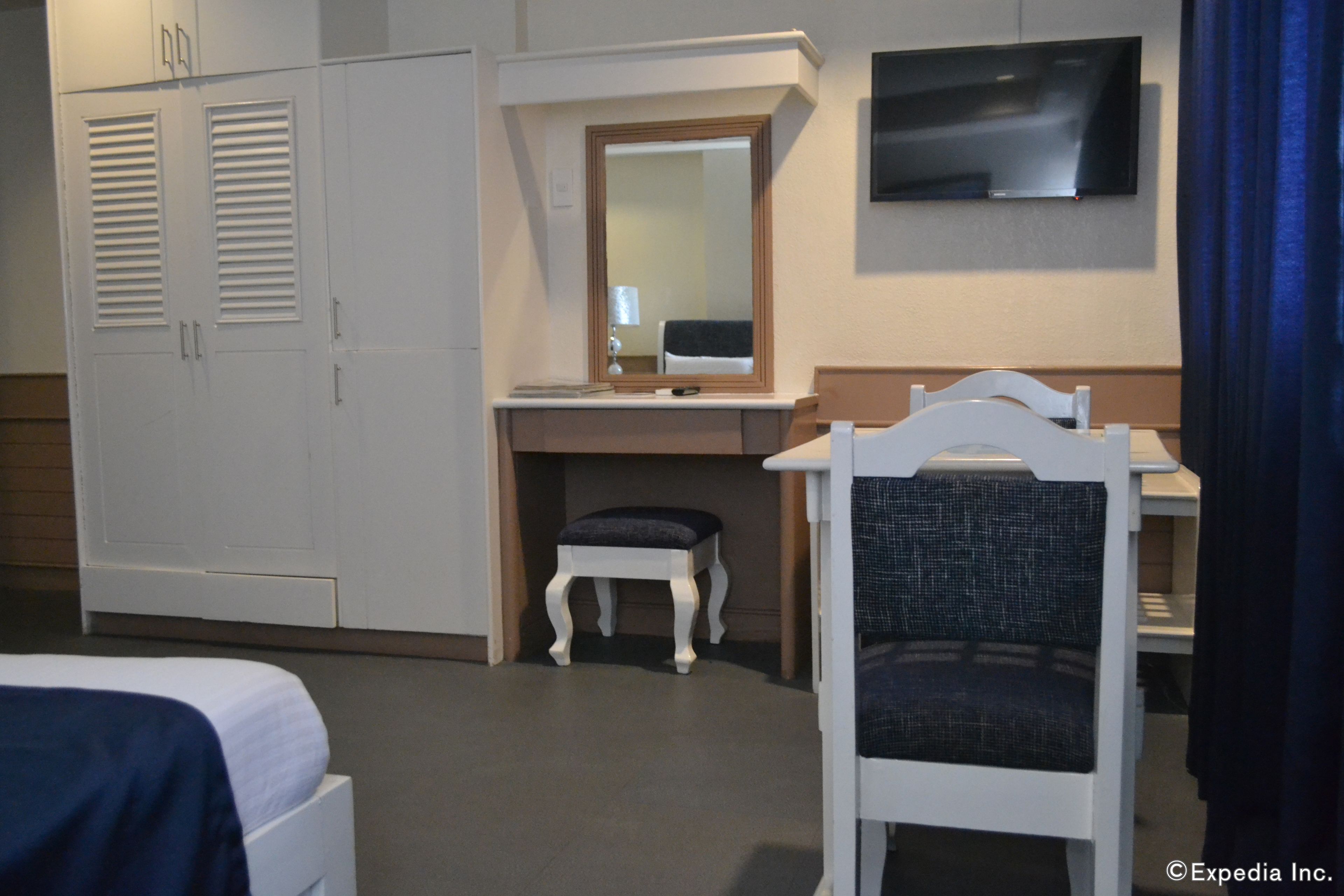 A hotel room with a bed, a desk with a chair, a television, and a wardrobe.