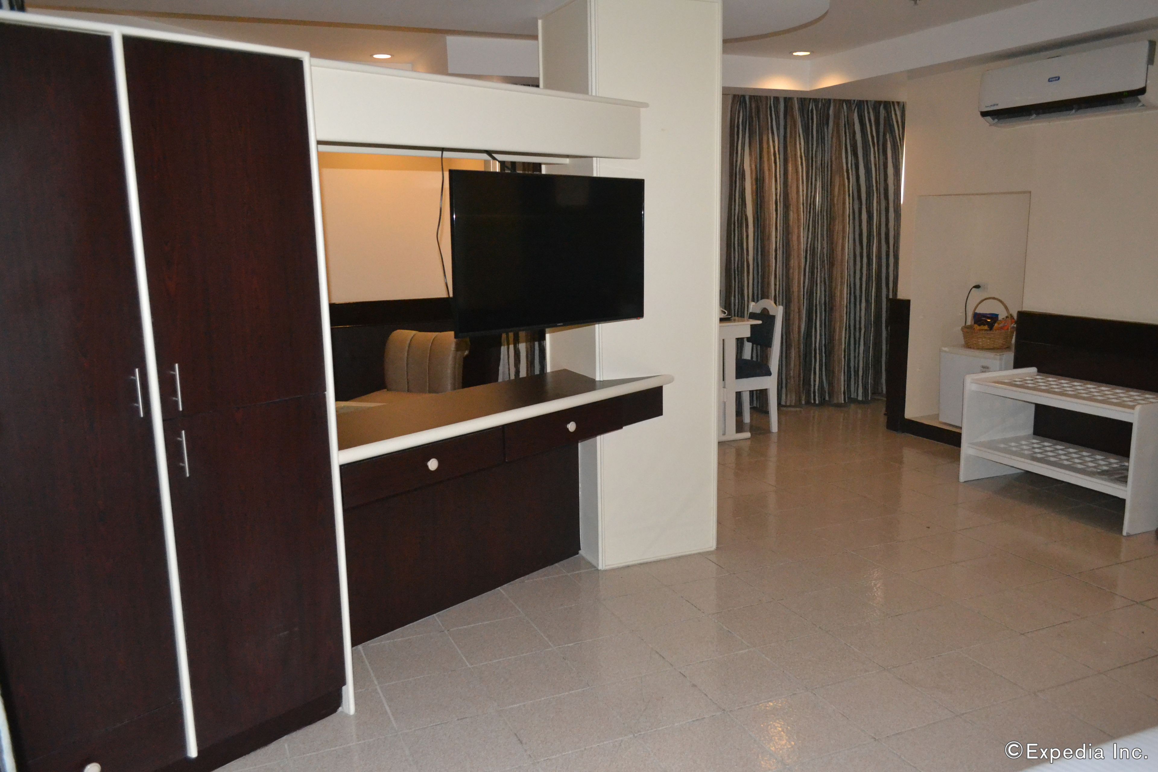 A modern hotel room with a flat-screen TV, a wardrobe, a desk, and a bed.