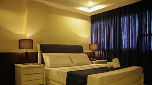 A hotel room with a bed, two bedside tables, lamps, a chair, and a large window with curtains. - Anchor Hotel (General Santos)
