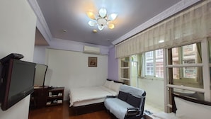 Quarto com cama, televisão, ventoinha no teto e janela com cortinas.