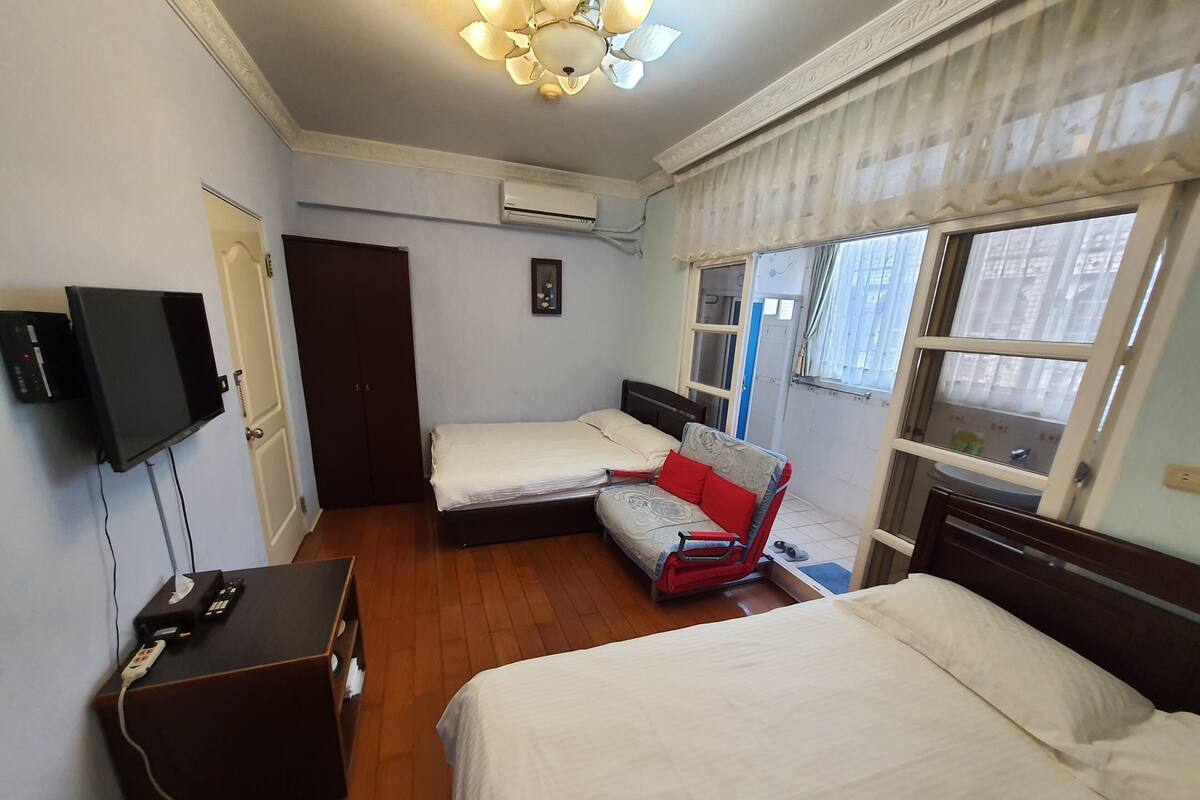 Ein Hotelzimmer mit zwei Betten, einer Schlafcouch, einem Fernseher und einer Klimaanlage.