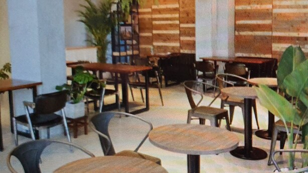 Interior de restaurante com mesas e cadeiras de madeira, plantas em vasos e uma parede de tijolos.
