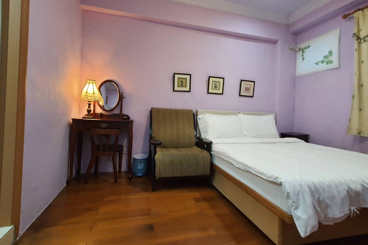 Ein Schlafzimmer mit Bett, einem Sessel, einem Schreibtisch mit Lampe und drei gerahmten Bildern an der Wand.