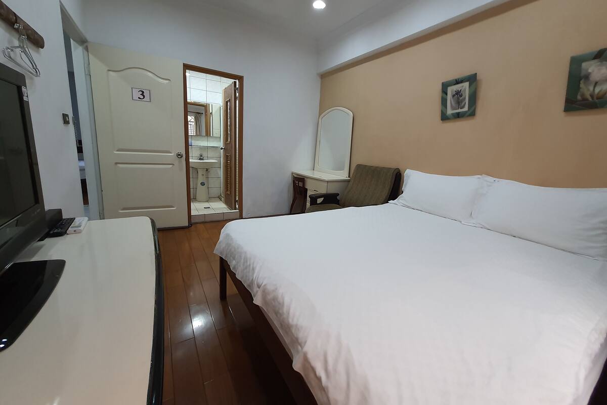 Ein Hotelzimmer mit Bett, Schreibtisch mit Stuhl, Fernseher und einem durch eine offene Tür einsehbaren Badezimmer.