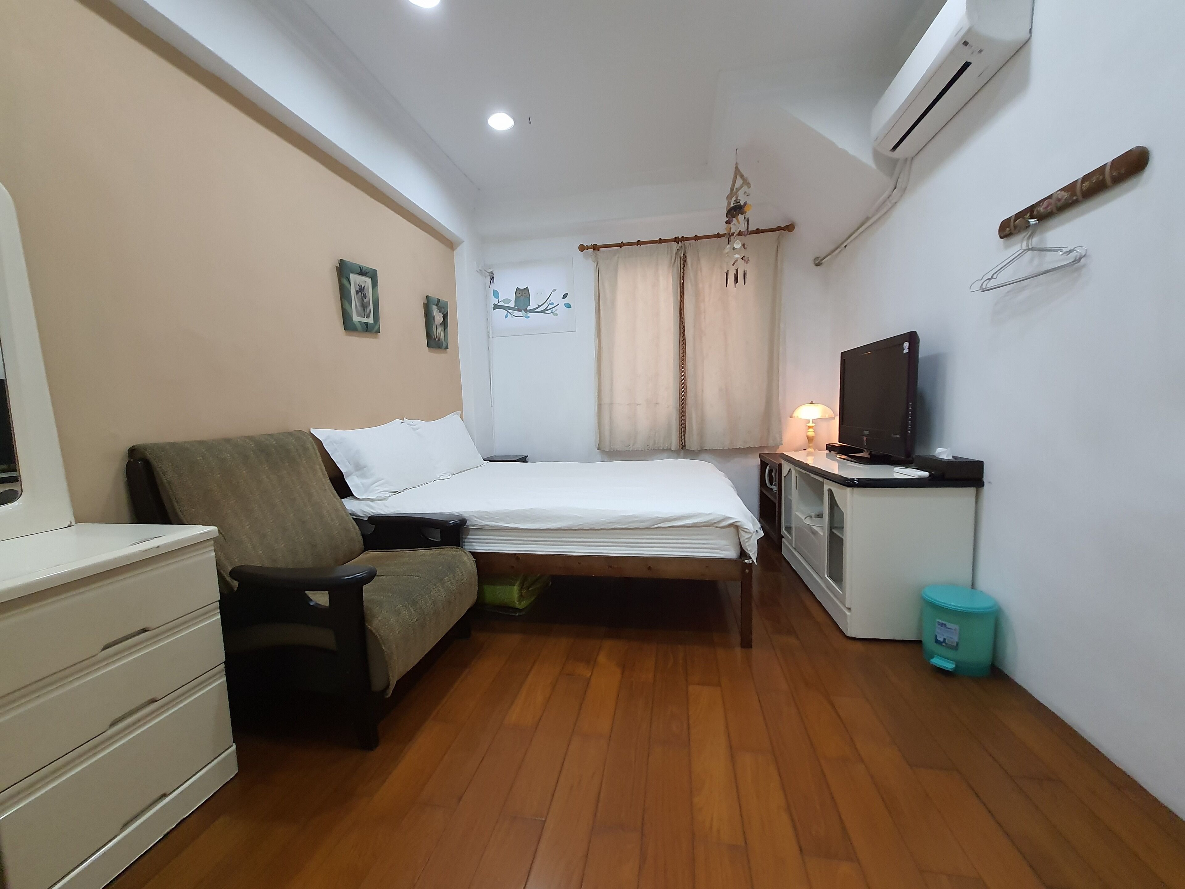 Una habitación pequeña y luminosa con cama, escritorio, computadora, silla, cómoda y un cesto de basura.