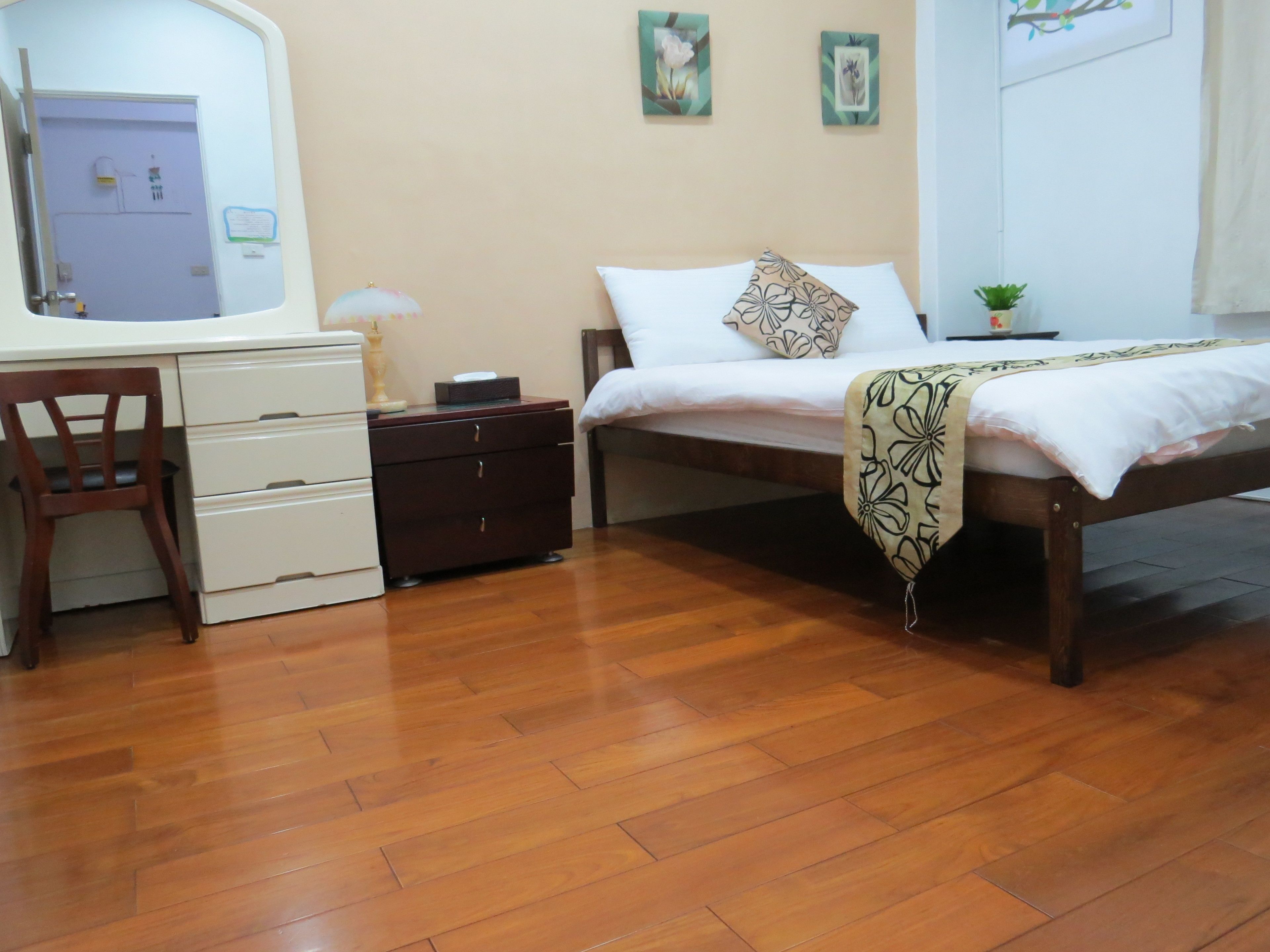 Un dormitorio con piso de madera, una cama con colcha estampada, un escritorio con silla y una pequeña planta en maceta.