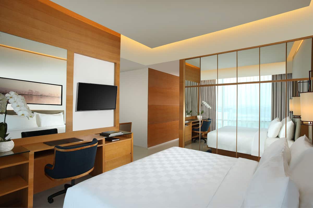A modern hotel room with a large bed, a desk with a chair, a flat-screen TV, and a large mirror.