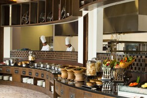 A buffet setup with multiple serving stations, a variety of dishes, and a chef in uniform. - Resinda Hotel Karawang, Managed by Padma Hotels (Karawang)