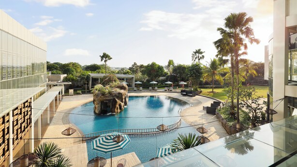 Un hôtel moderne doté d’une grande piscine extérieure, entouré de palmiers et d’un jardin bien entretenu.