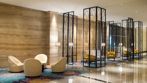 Un hall d’entrée doté d’un sol en marbre poli, d’un grand mur recouvert de panneaux en bois et d’un espace détente avec des fauteuils modernes et un fauteuil jaune.