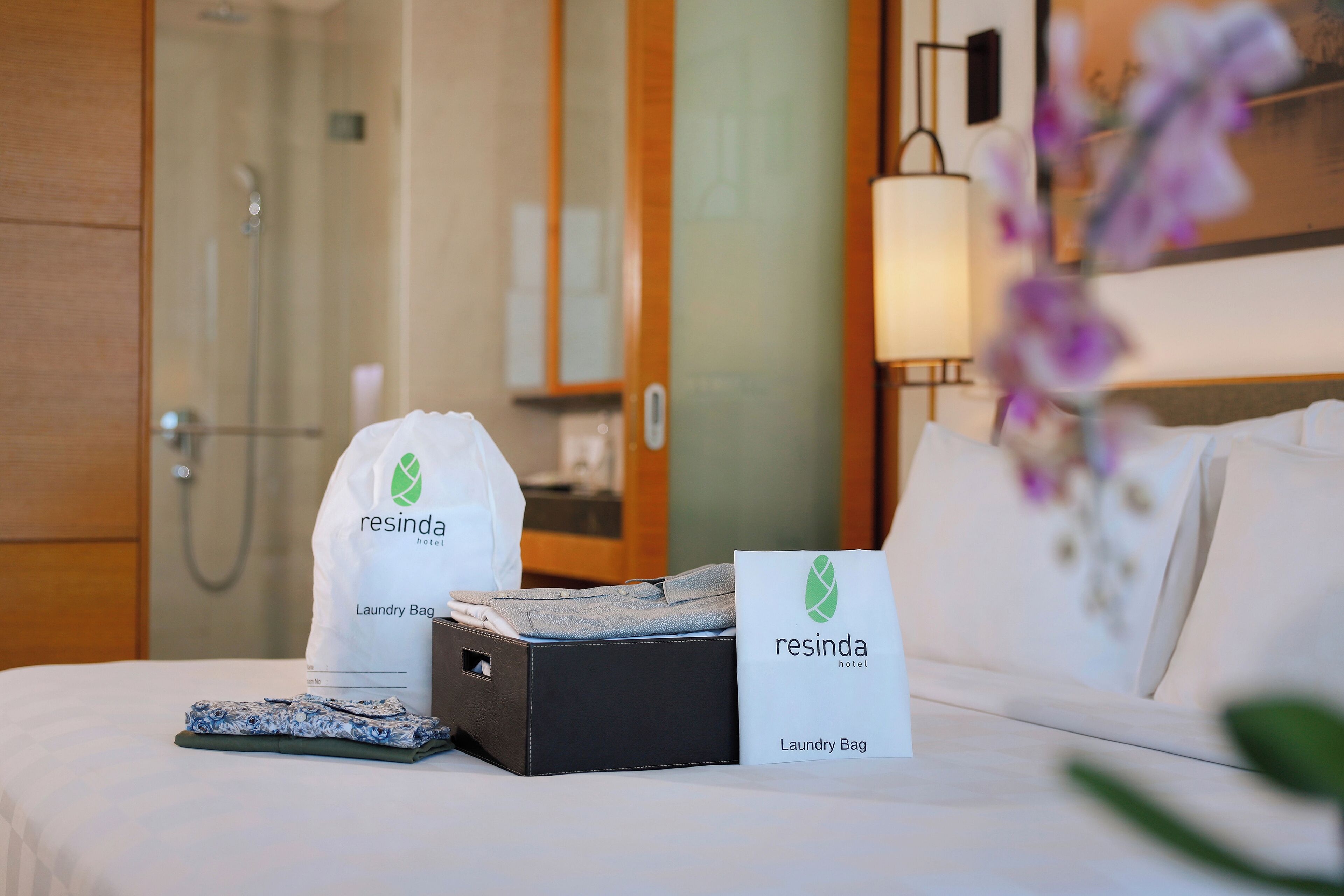 A hotel room with a neatly made bed, a laundry bag, and a box of toiletries.