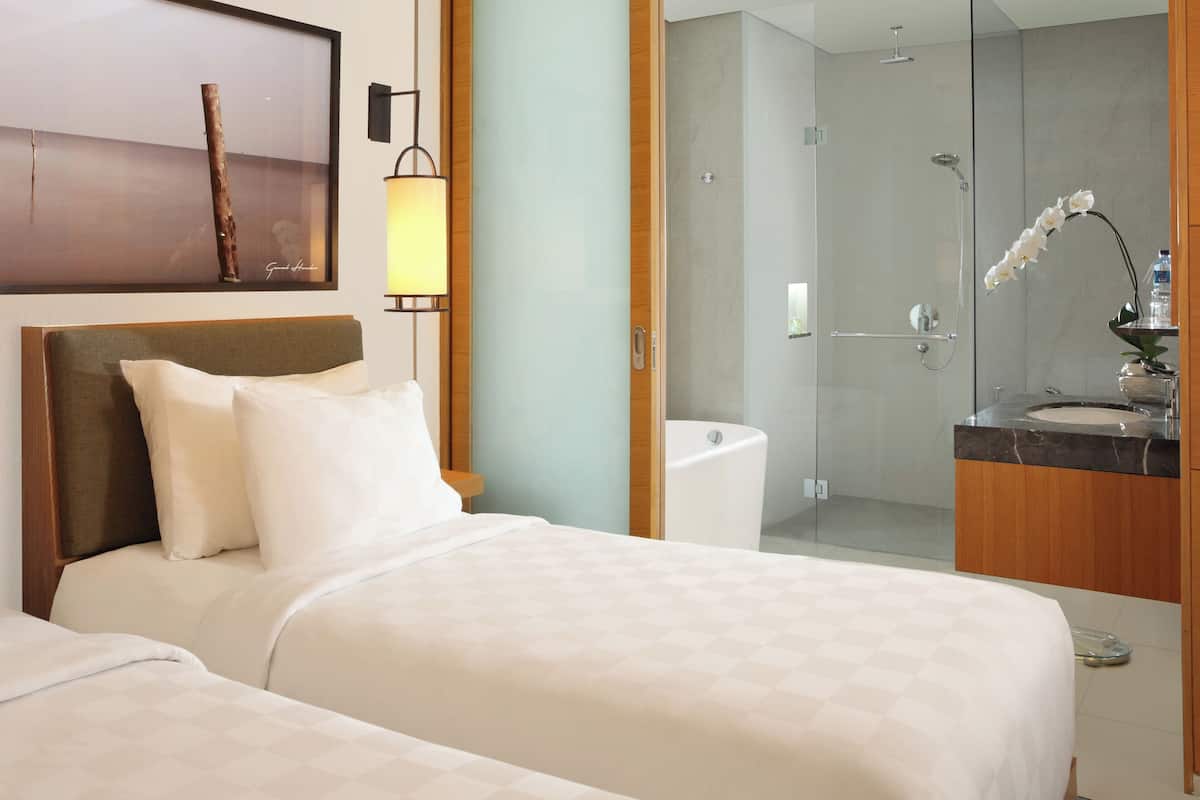 A hotel room with a bed, a bedside table, a lamp, a bathroom with a shower, and a mirror.