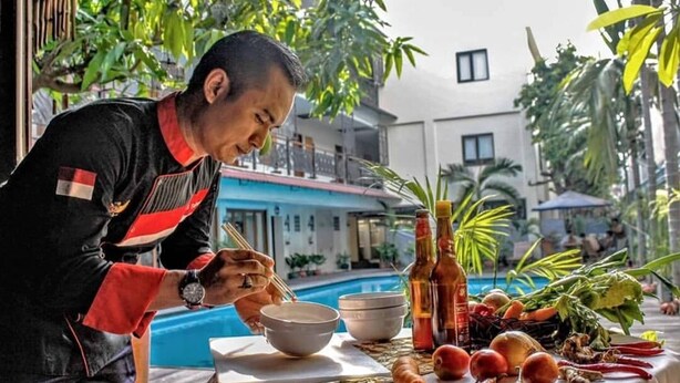 Une personne prépare des aliments à l’extérieur, sur une table où sont disposés des bols, des bouteilles et des légumes frais.