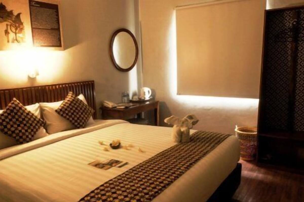 Una habitación de hotel con una cama, una mesita de noche, una lámpara, un espejo y una ventana.