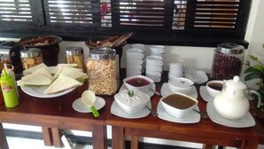 Un buffet de petit-déjeuner avec des sandwichs, diverses sauces et des boissons, le tout disposé sur une table en bois.