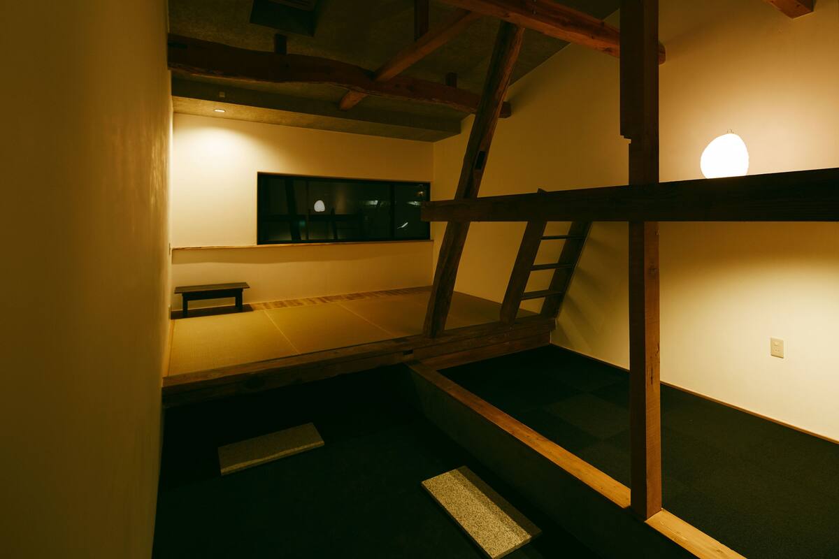 A bunk bed with a ladder, a small shelf, and a wall-mounted light fixture.