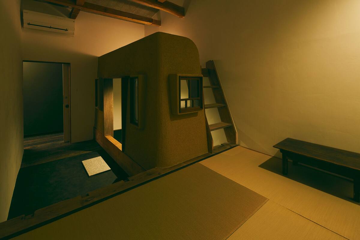 A room with a sloped ceiling, a ladder, a bench, and a door.