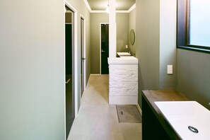 A narrow hallway with a white sink and a mirror on a white pedestal, leading to a dark room.