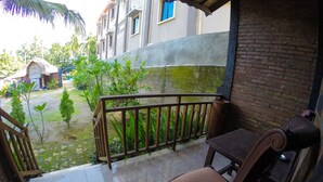 A balcony with a wooden chair and a table, a tiled floor, a brick wall, and a view of a residential area with houses and greenery. - Warungku In Home Stay Senggigi (Senggigi)