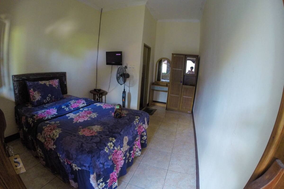 Ein Schlafzimmer mit einem Bett, einem Nachttisch, einem an der Wand montierten Fernseher und einem Kleiderschrank.